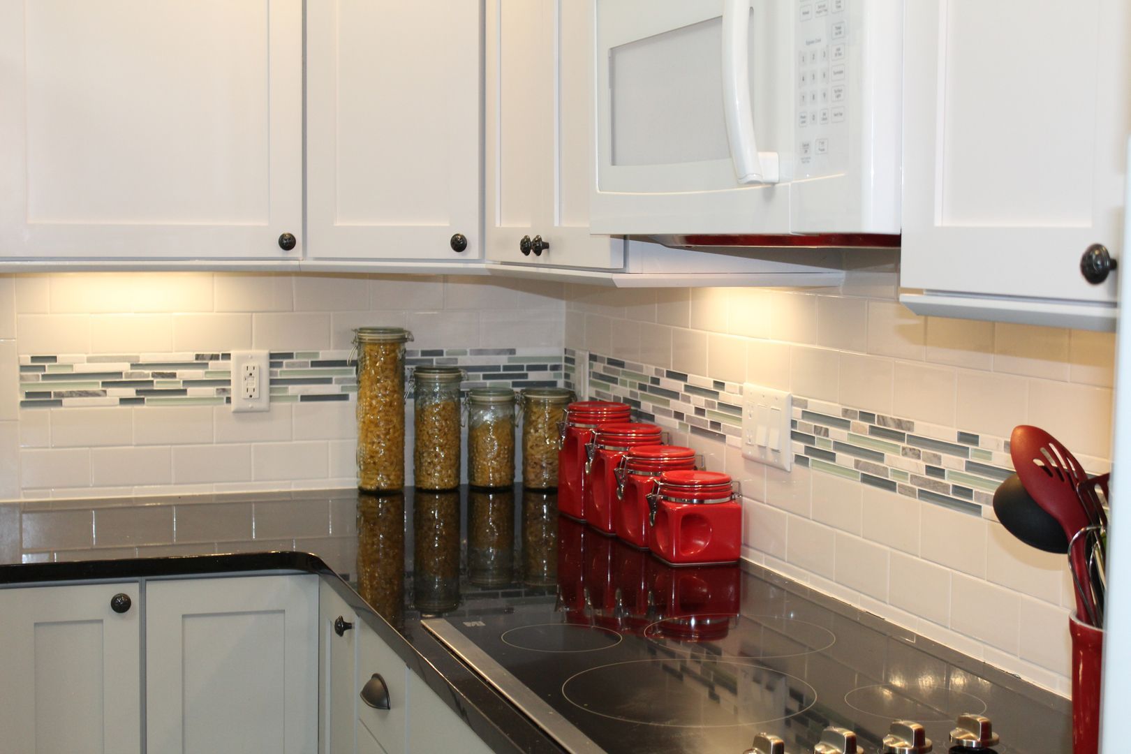 Kitchen countertop with jars and red containers under white cabinets and a microwave