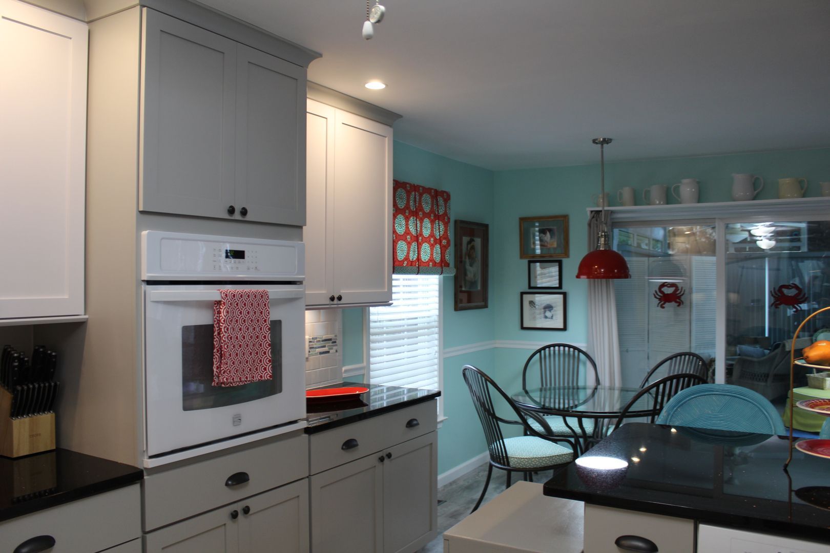 Bright kitchen and dining area with white cabinets, glass table, teal chairs, and red pendant light