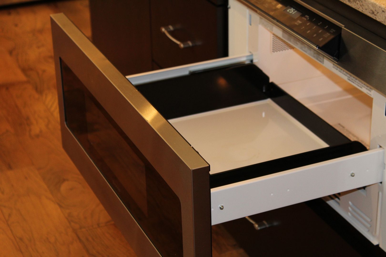 Open drawer with white front and black interior in a wooden kitchen cabinet