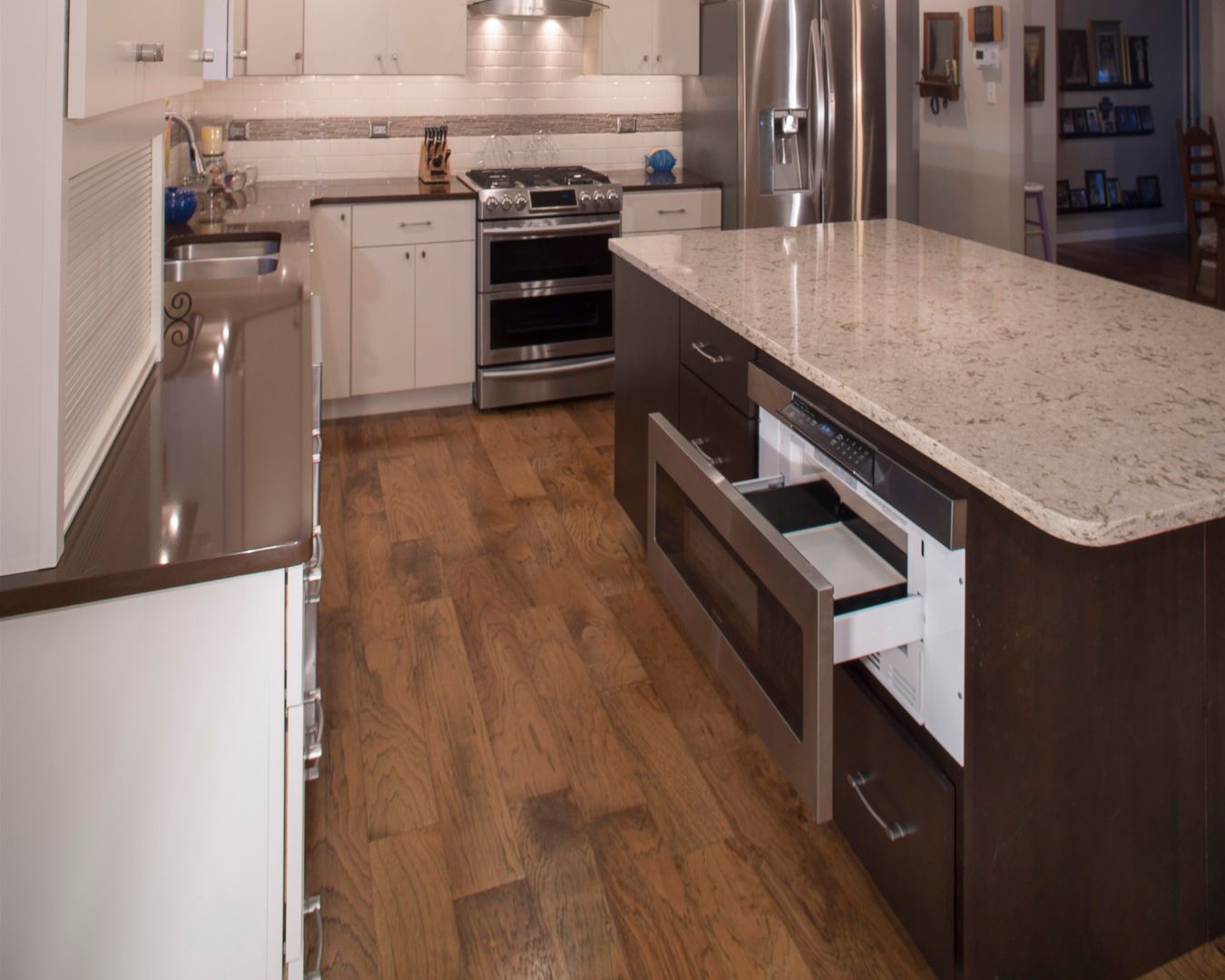 Modern kitchen with wood floors, white cabinets, stainless appliances, and a granite island counter.