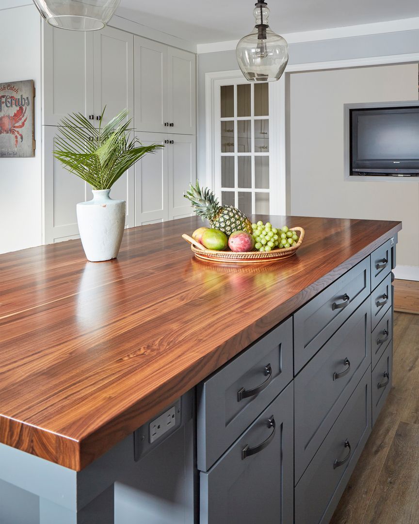 Kitchen island with a wooden countertop, gray drawers, a white vase of flowers, and a fruit bowl in a bright kitchen