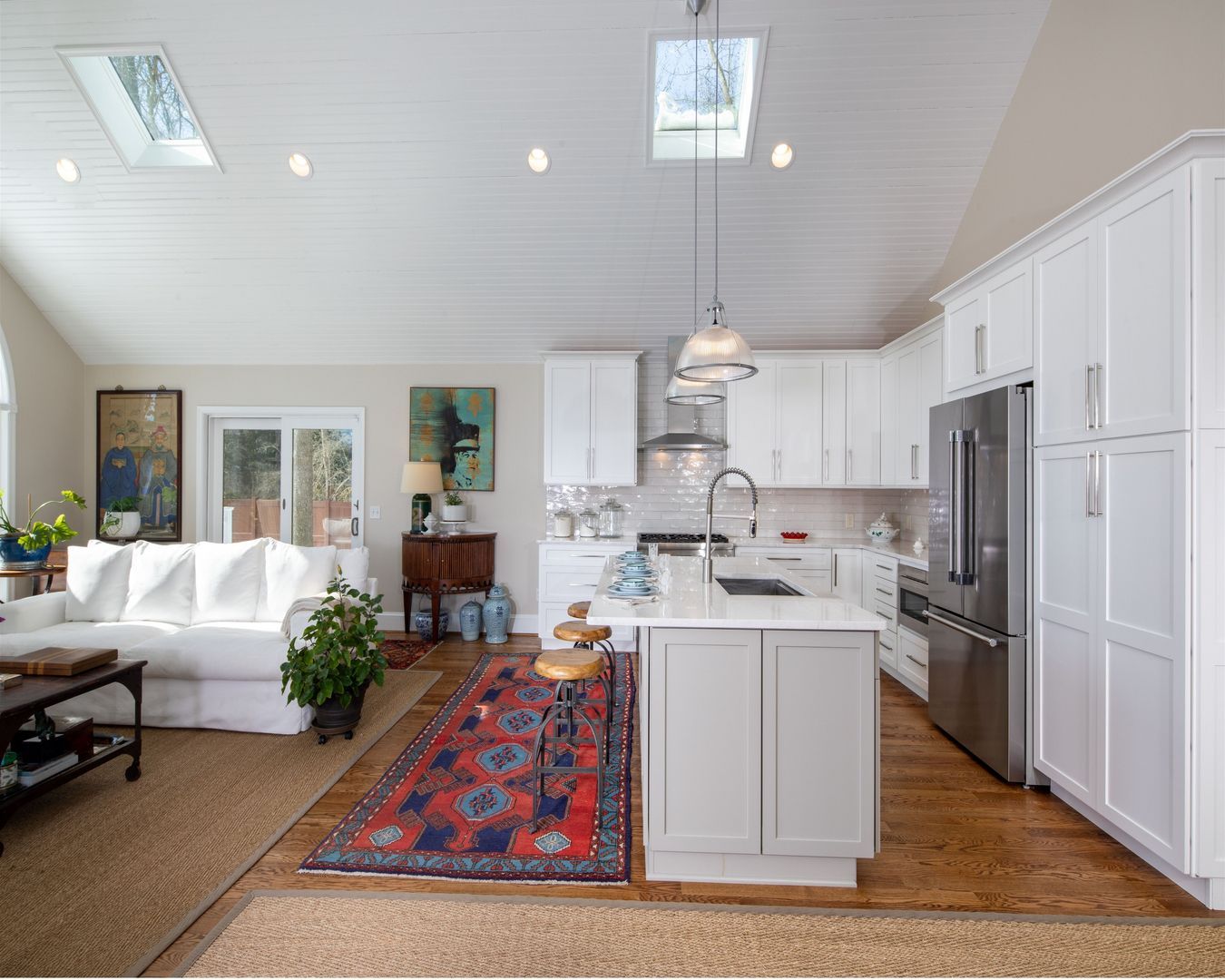 Bright open living room and kitchen with white furniture, island, skylights, and a colorful runner rug