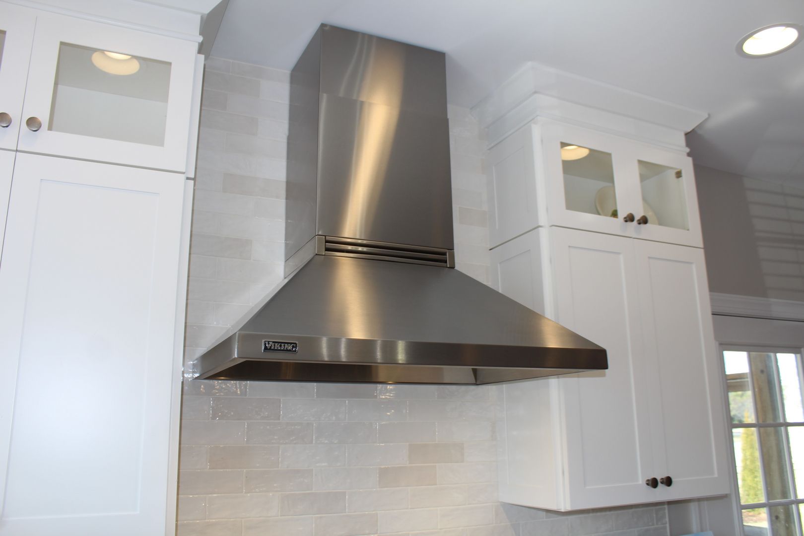 Modern kitchen with stainless steel range hood, white cabinets, and light tile backsplash