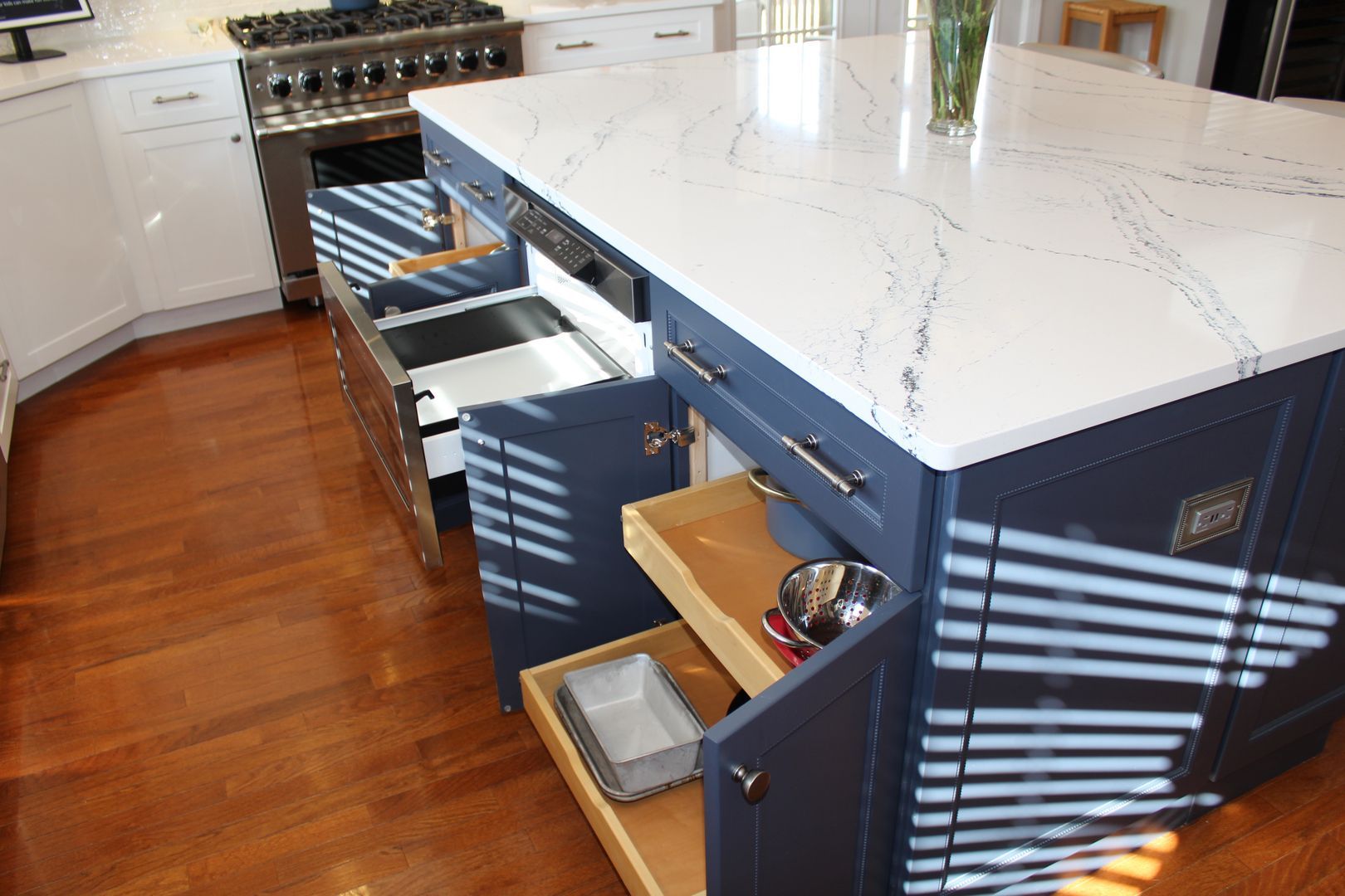 Modern kitchen island with white countertop, blue cabinets, and open drawers on a hardwood floor