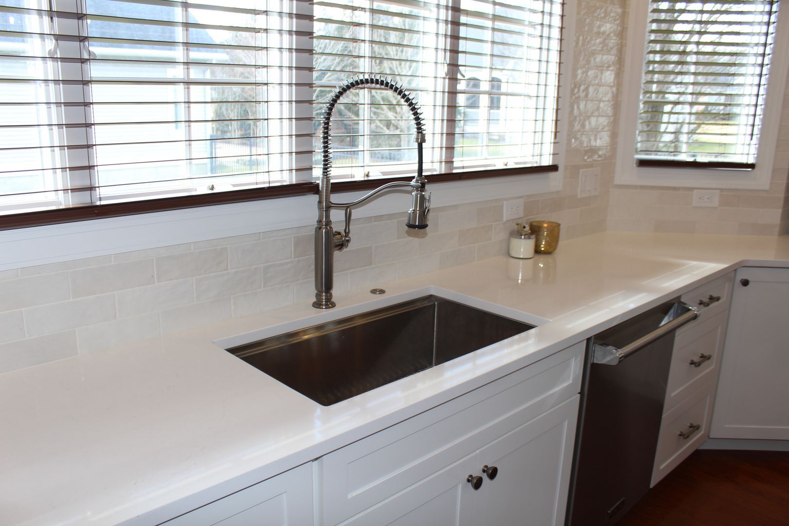 Modern kitchen countertop with stainless sink, chrome faucet, white cabinets, and window blinds