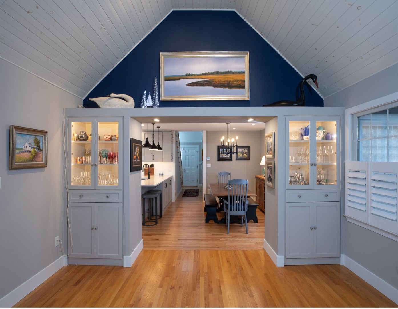 Bright dining room with vaulted blue ceiling, white cabinets, wood floors, and a view into the kitchen.