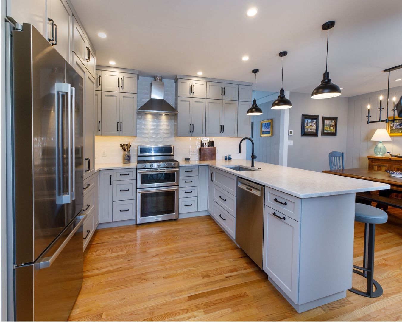 Bright modern kitchen with stainless steel appliances, gray cabinets, wood floors, and a white island
