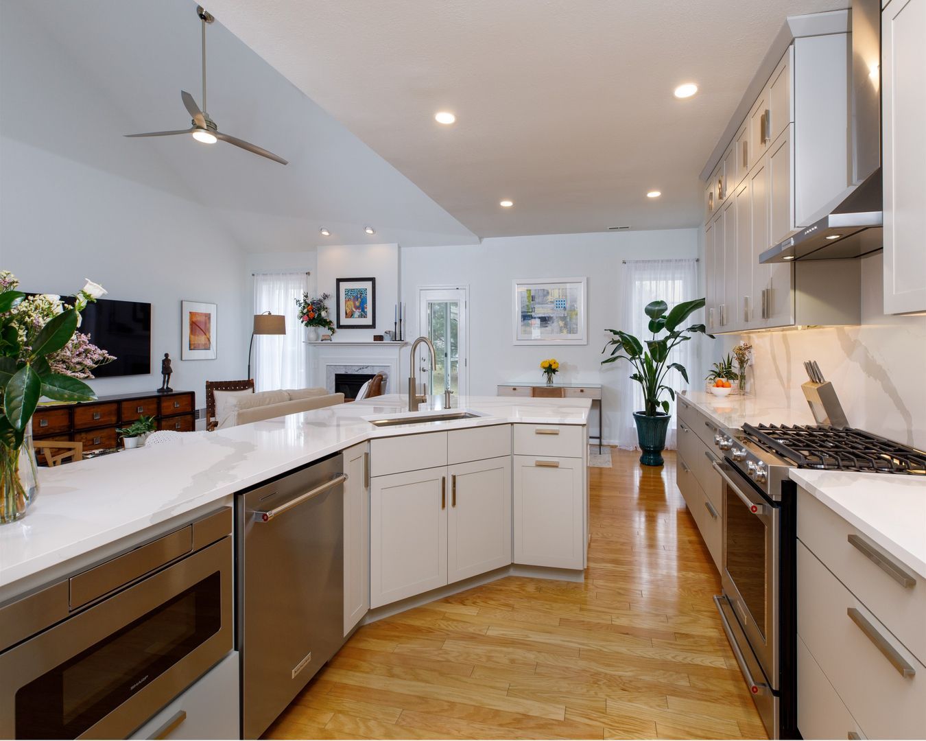 Bright modern kitchen with white cabinets, marble island, wood floors, and stainless steel appliances