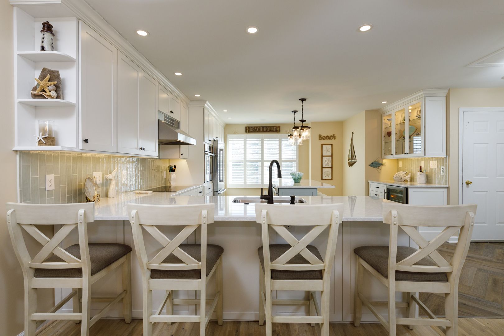 Bright white kitchen with island seating, pendant lights, and a large window in the background