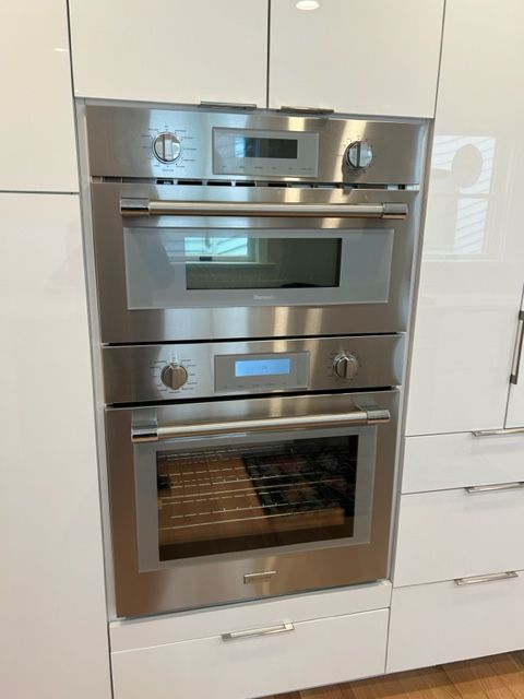 Built-in stainless steel oven and microwave stack in a white kitchen cabinet.