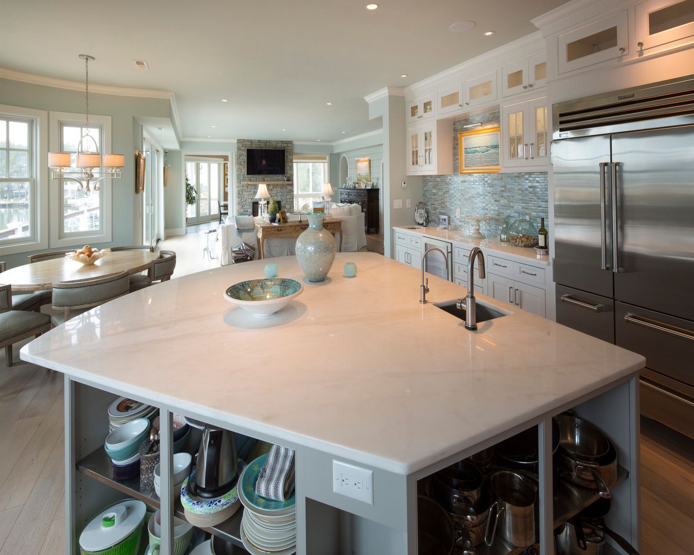 Bright modern kitchen with large island, stainless steel fridge, white cabinetry, and open shelves.