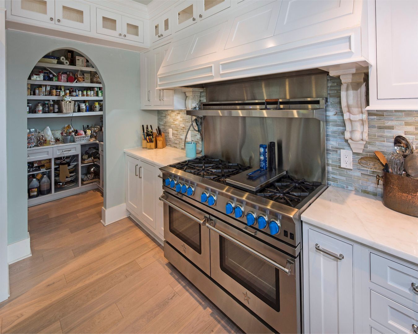 Bright modern kitchen with stainless steel stove, white cabinets, and arched pantry shelves