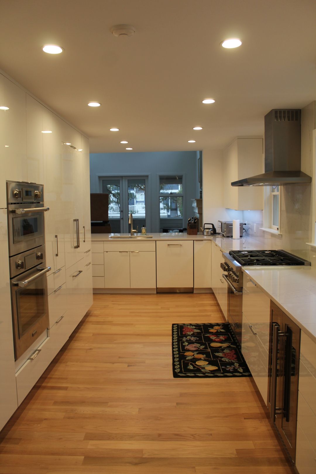 Modern white kitchen with wood floors, stainless appliances, and a window over the sink