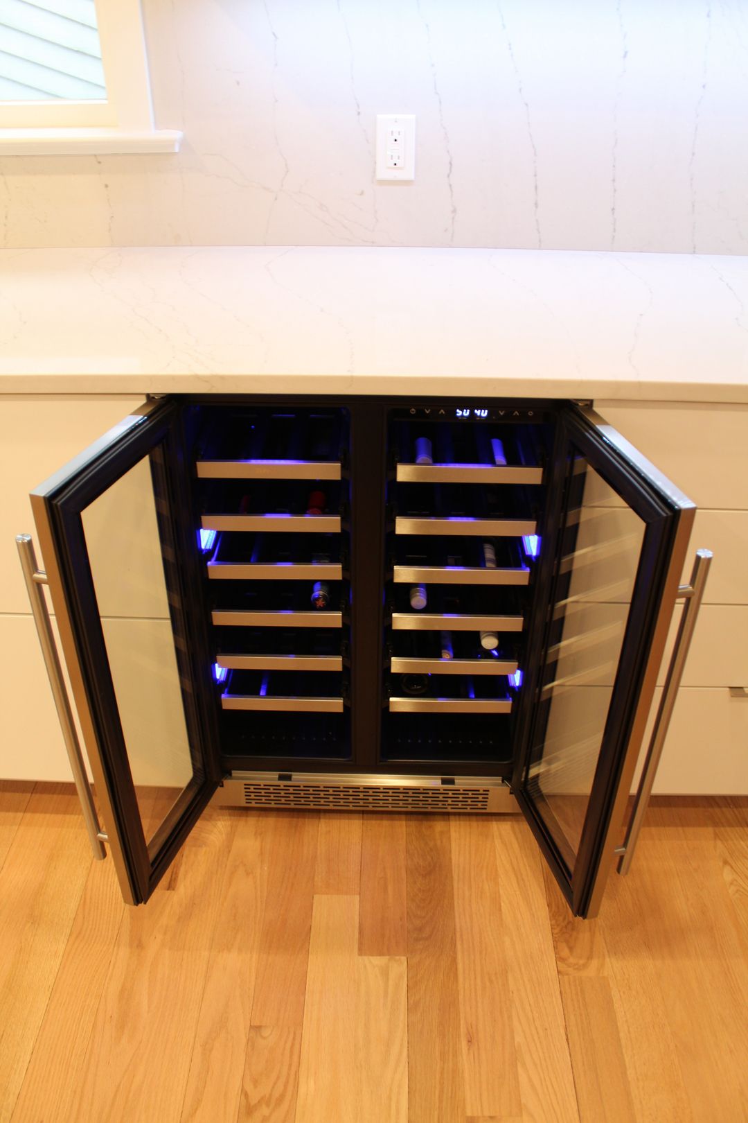 Open black wine fridge with wooden shelves in a kitchen beside a counter.