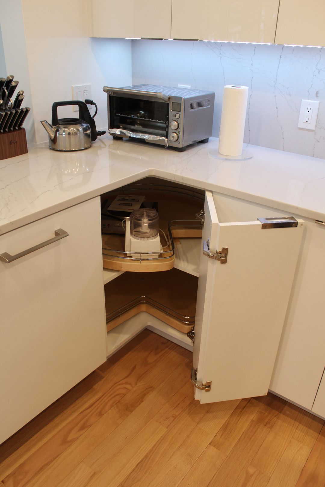 Open corner kitchen cabinet revealing a mixer on a wooden Lazy Susan shelf.
