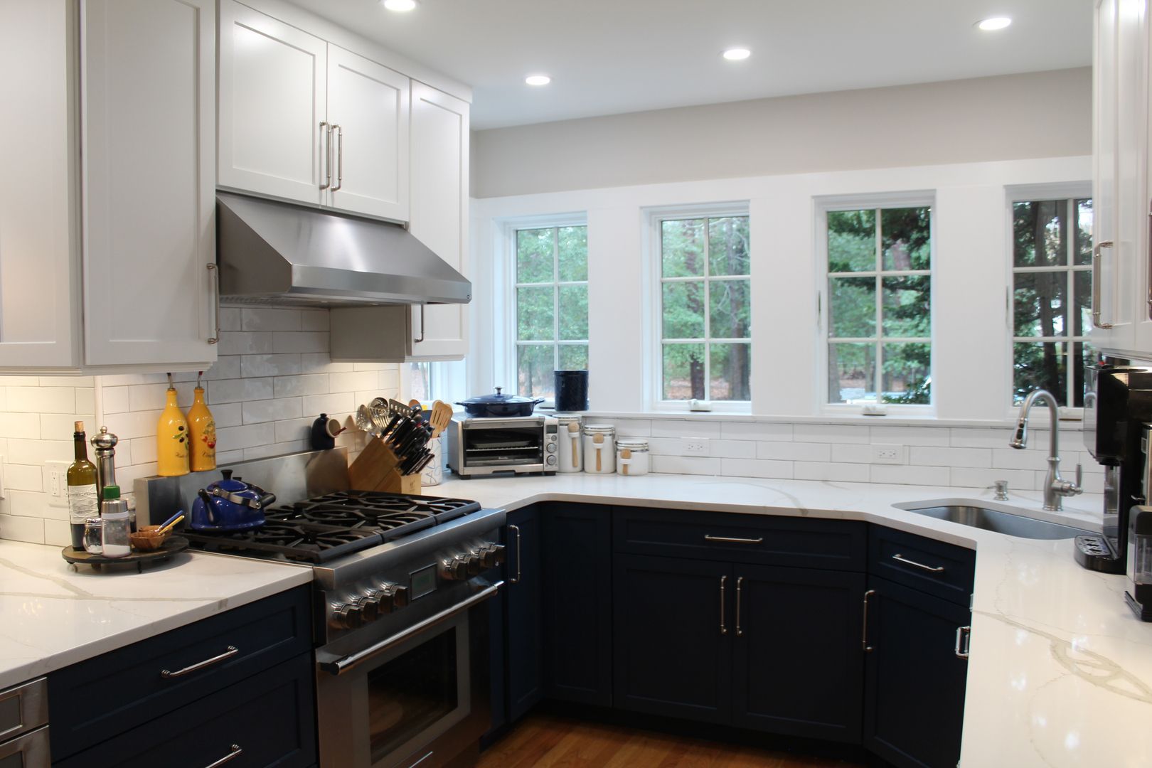 Modern white kitchen with black lower cabinets, stainless stove, and large windows over a sink.