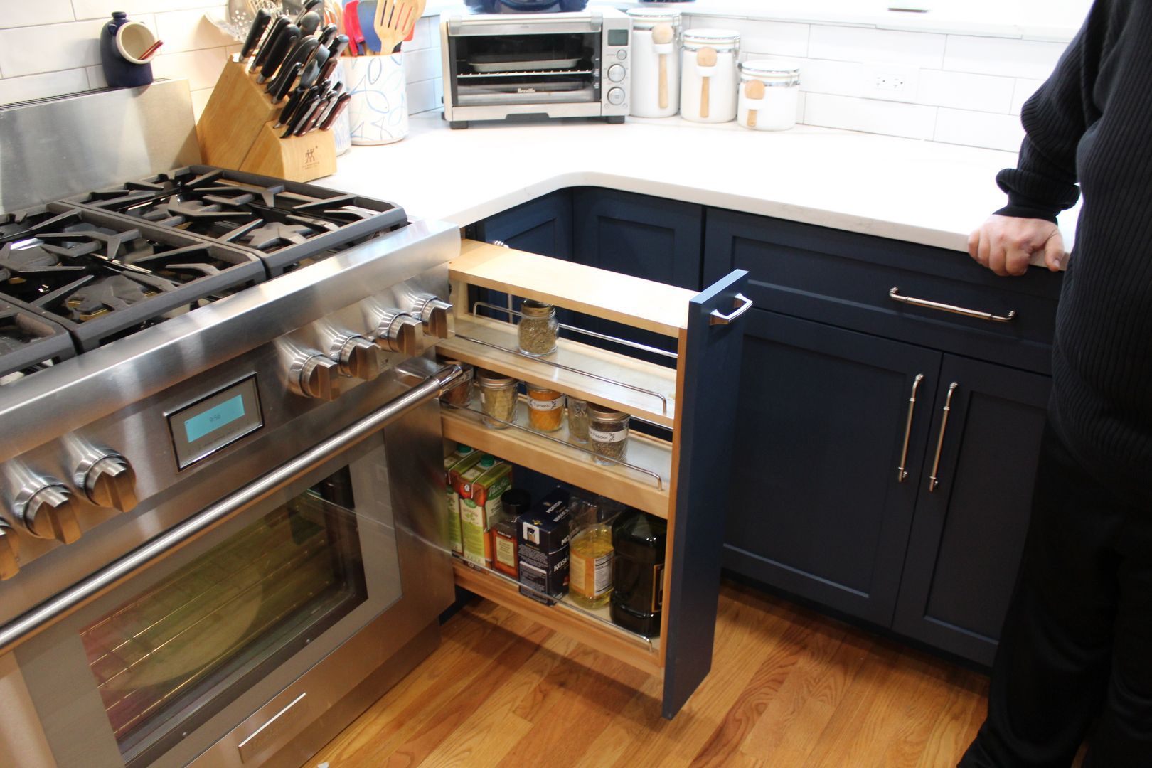 Modern kitchen corner with open drawers, stove, oven, and black cabinets next to a white countertop