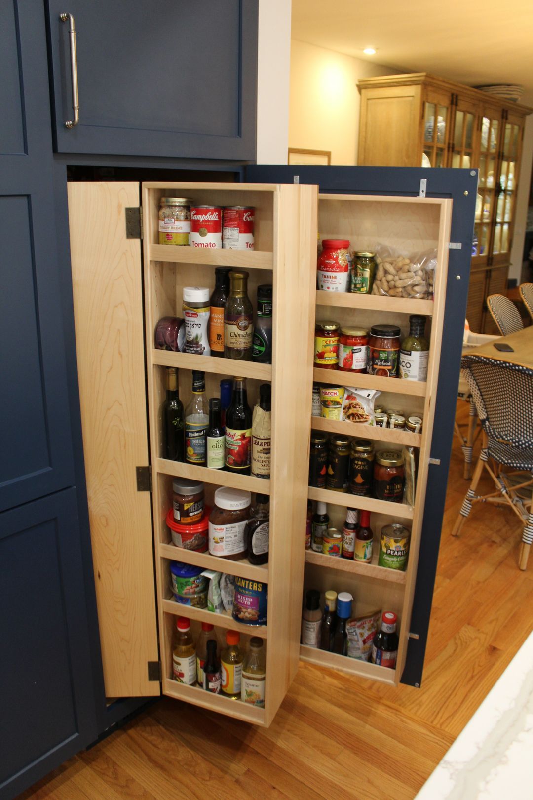Open pantry cabinet with shelves of canned goods and spices in a kitchen.