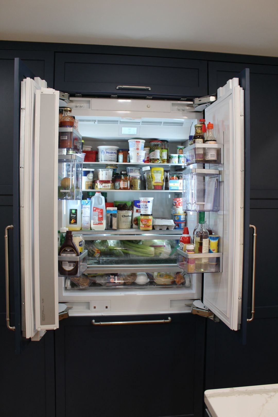Open refrigerator packed with food and containers in a dark kitchen.