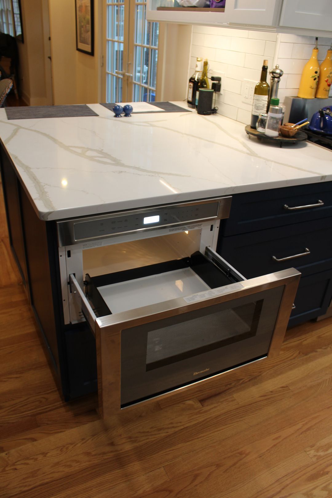 Modern kitchen with a large white island countertop and an open oven drawer below.