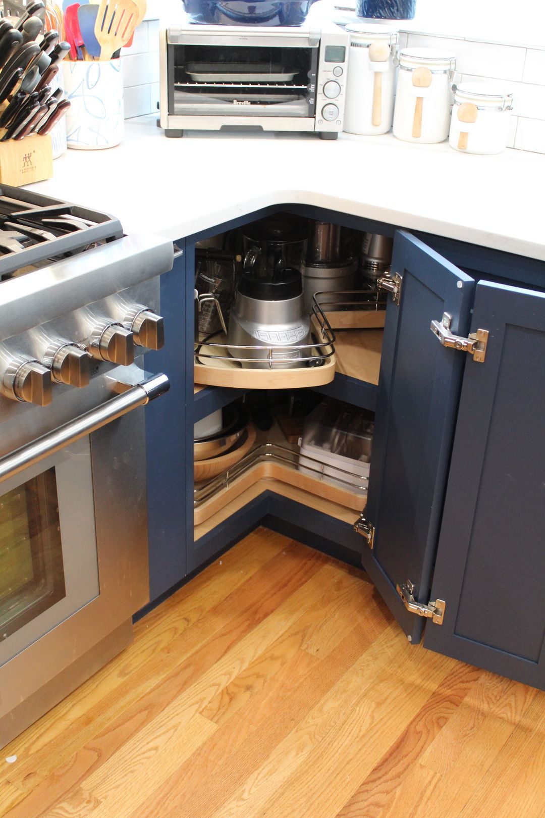 Corner kitchen cabinet with pull-out shelves holding pots and pans, next to an oven and hardwood floor.