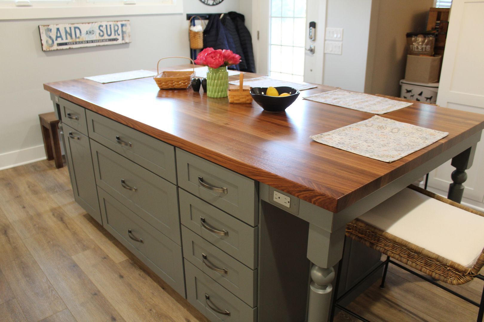 Kitchen island with wooden countertop, gray drawers, and place settings in a bright dining space