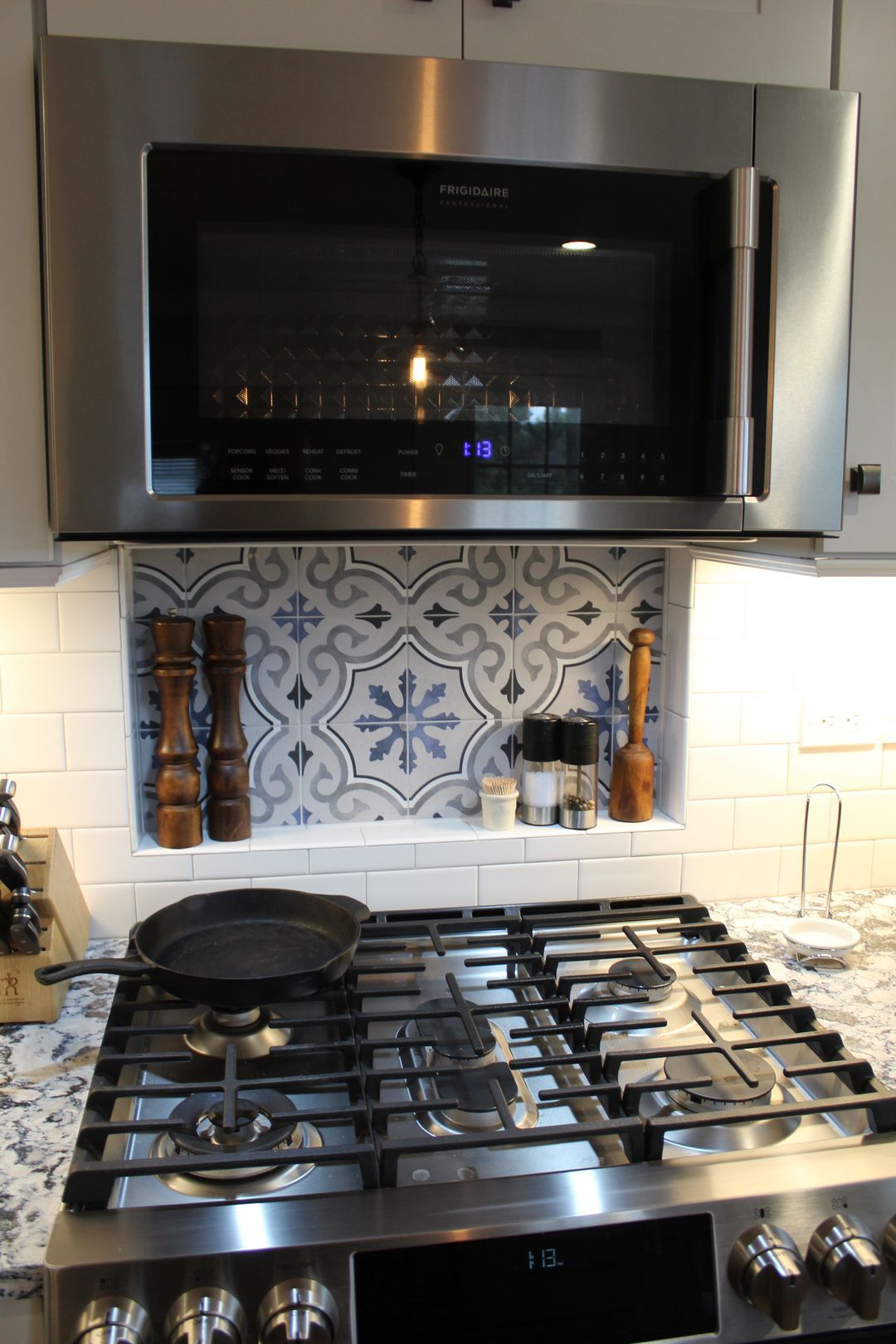 Stainless steel stove with pans beneath a microwave in a tiled kitchen.