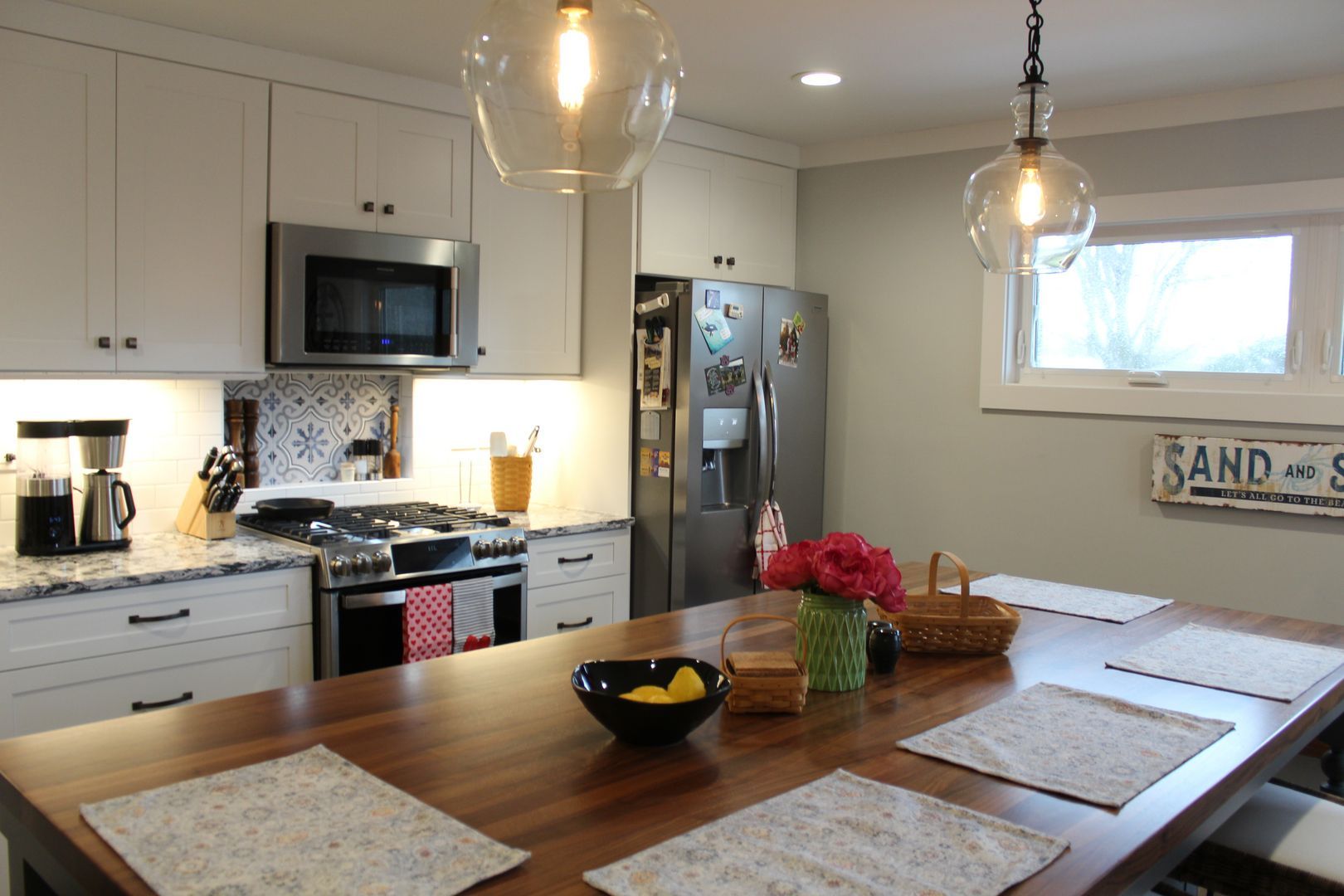Modern kitchen with wooden dining table, white cabinets, stainless appliances, and pendant lights