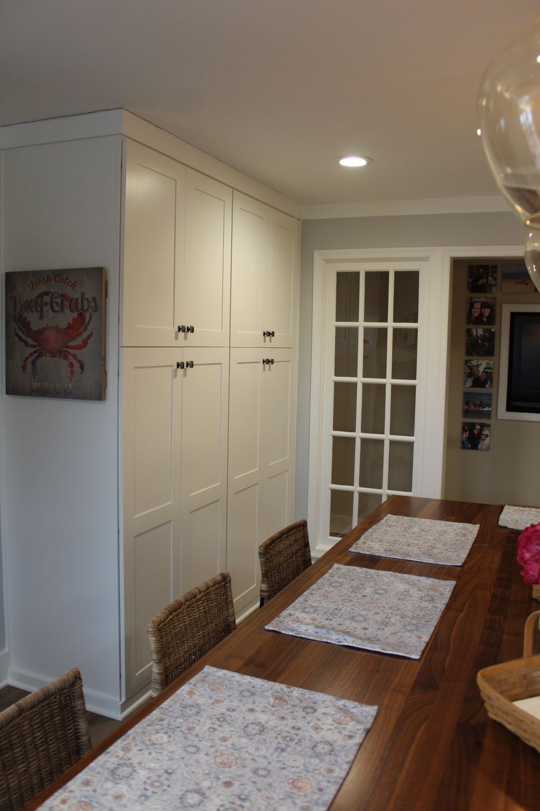 Dining room with long wooden table, white cabinets, and glass-paned doors under recessed lighting