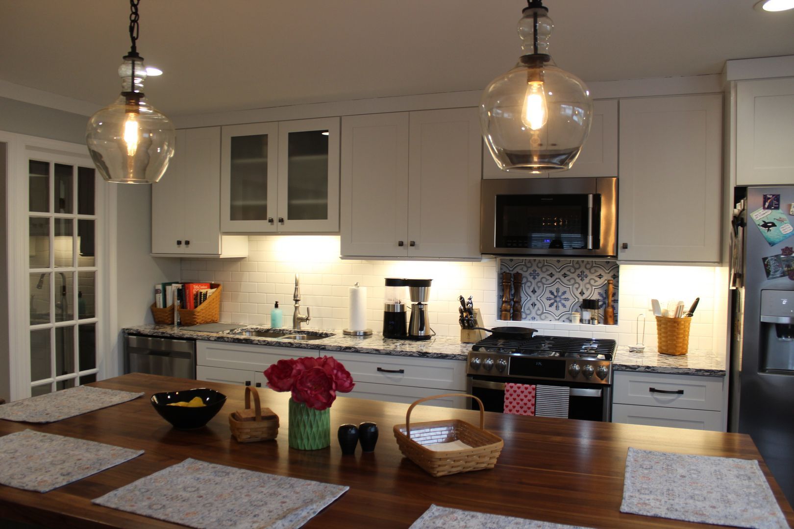 Bright modern kitchen with white cabinets, stainless appliances, and a wooden island with flowers and placemats.