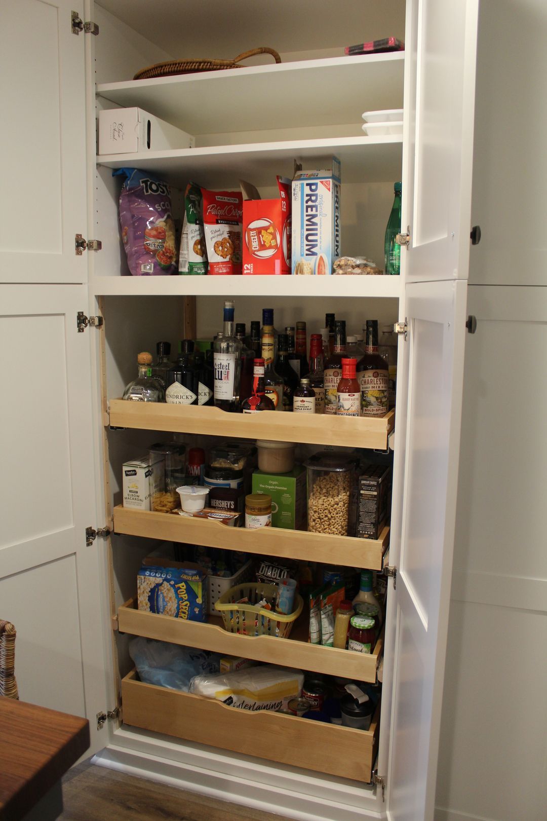 Open pantry cabinet with shelves of snacks, bottles, and jars, plus a pull-out organizer below.