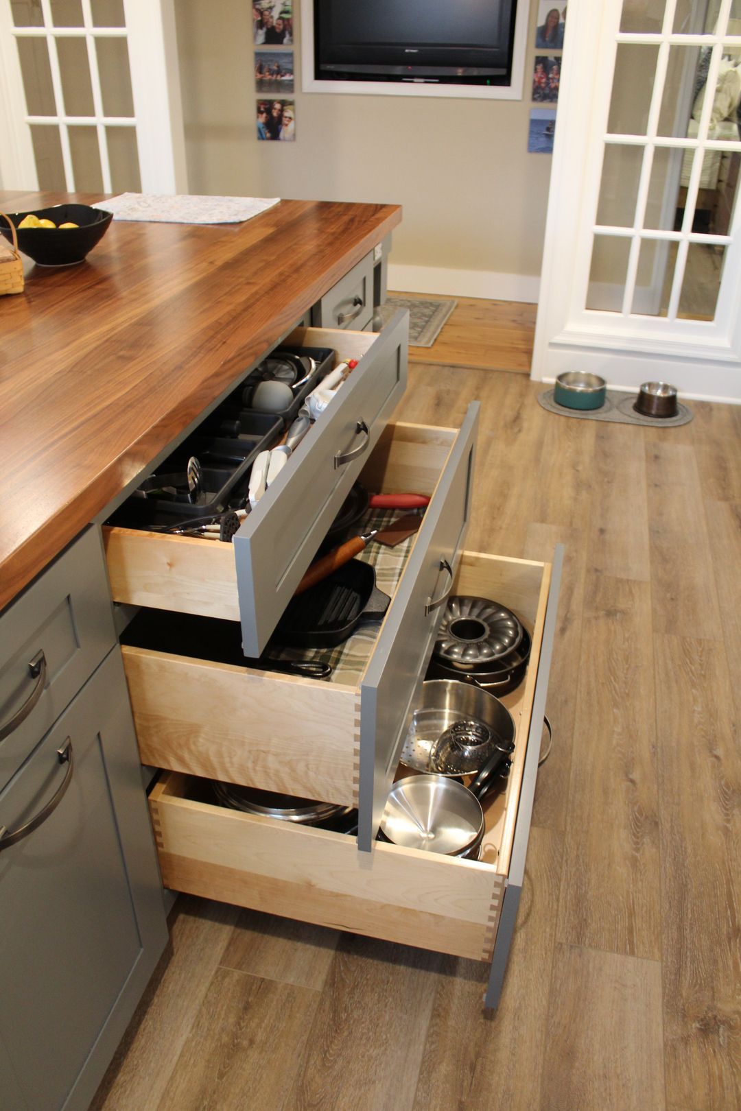 Kitchen island drawer organizers with pots, bowls, and utensils pulled open in a home kitchen