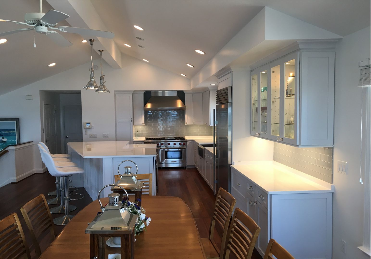 Modern open-plan kitchen with white cabinets, dark wood floors, and pendant lights, viewed from the dining area