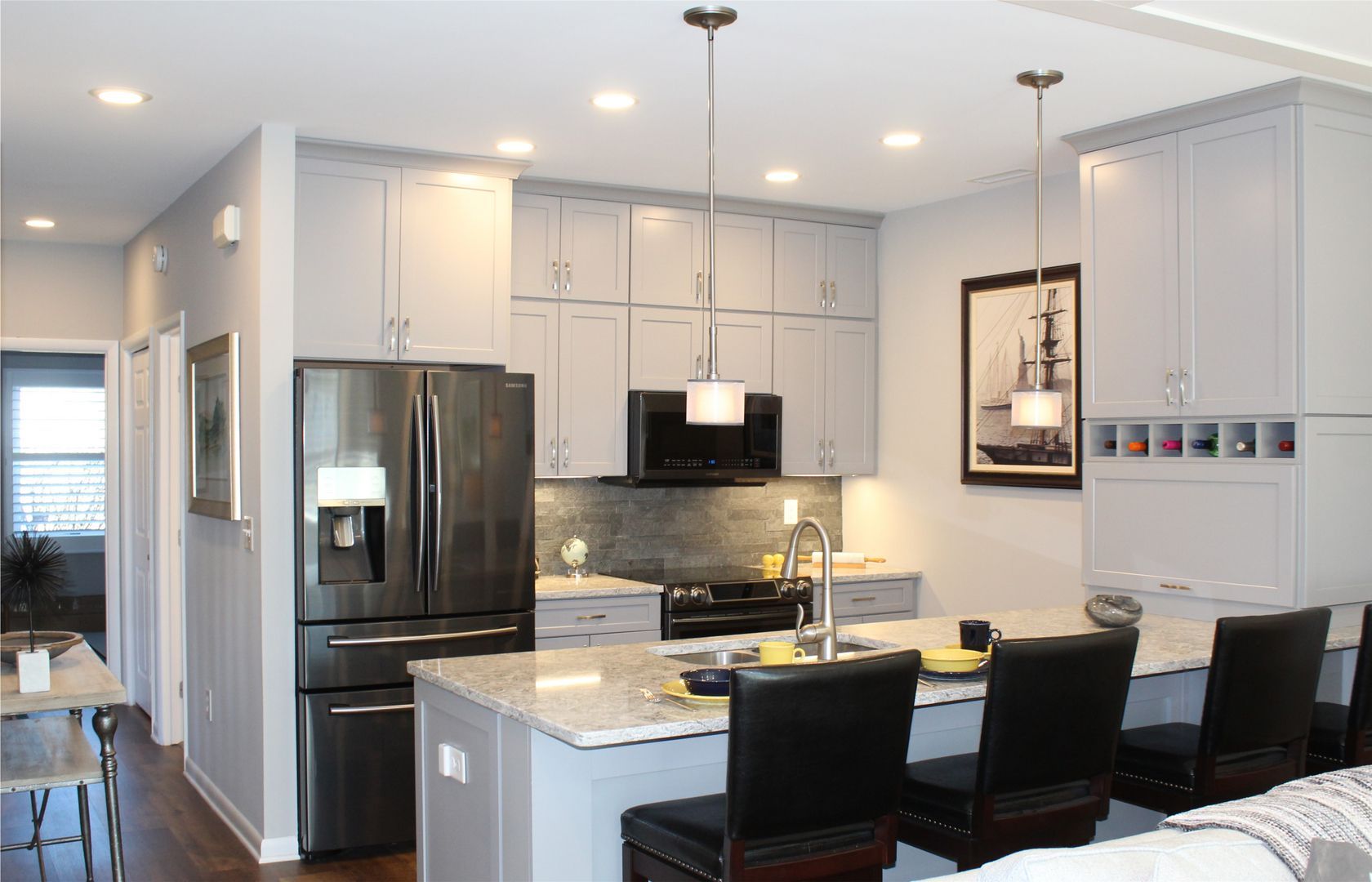 Modern kitchen with stainless appliances, white cabinets, island, and black bar stools under pendant lights