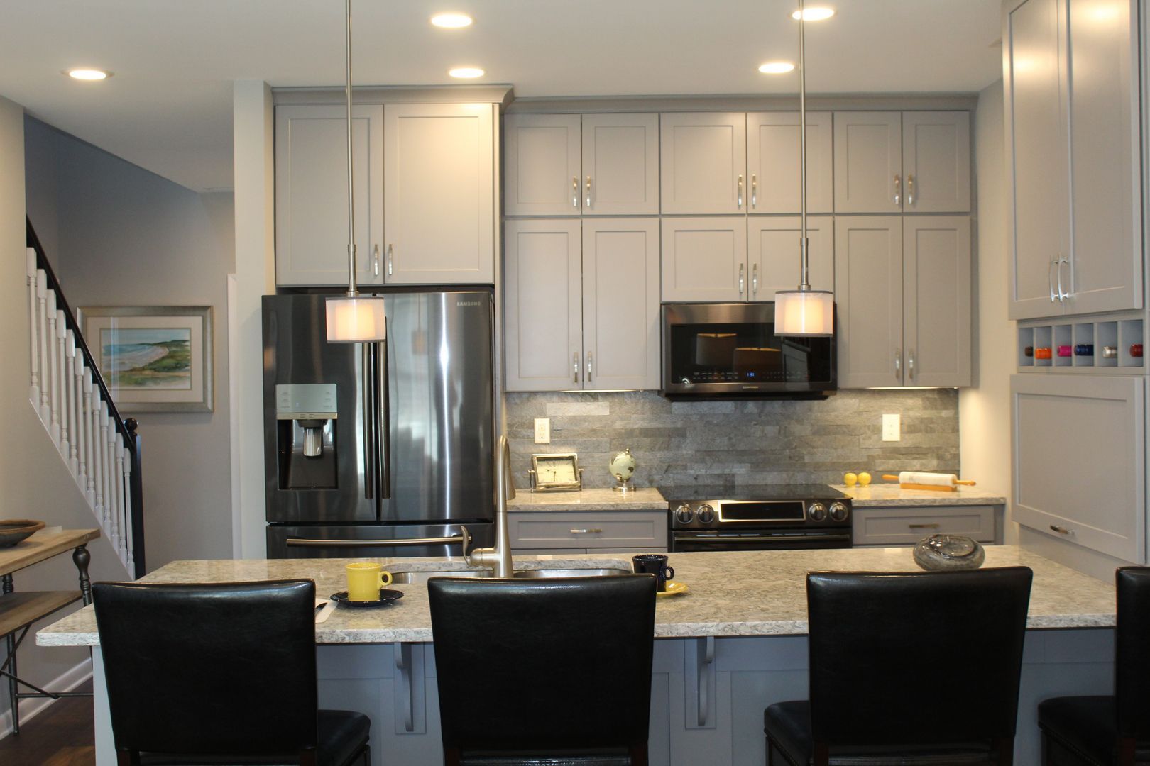 Modern kitchen with white cabinets, stainless steel appliances, and a granite island with three black chairs