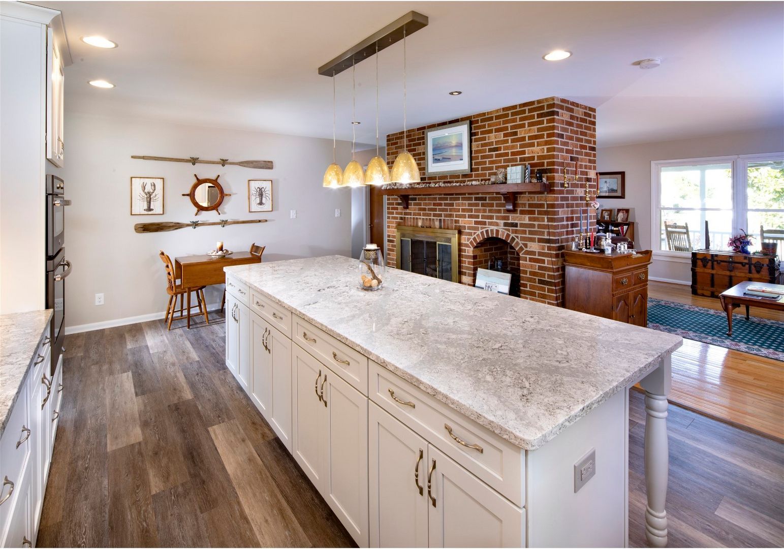 Bright open kitchen with large island, pendant lights, brick fireplace, and dining area beyond