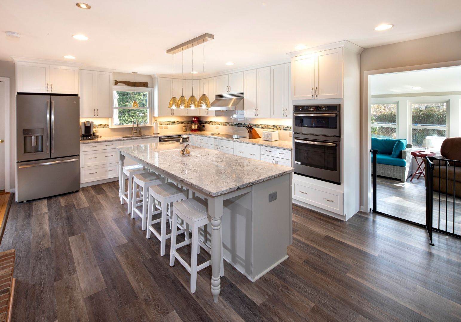 Bright modern kitchen with white cabinets, marble island, stainless appliances, and dark wood floors