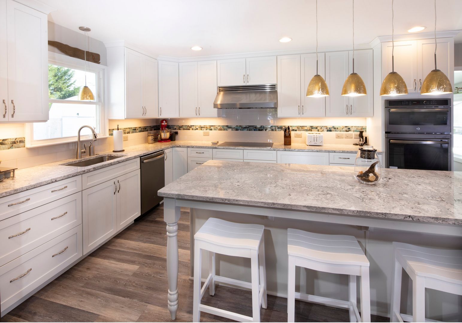 Bright modern kitchen with white cabinets, granite island, pendant lights, and two stools.