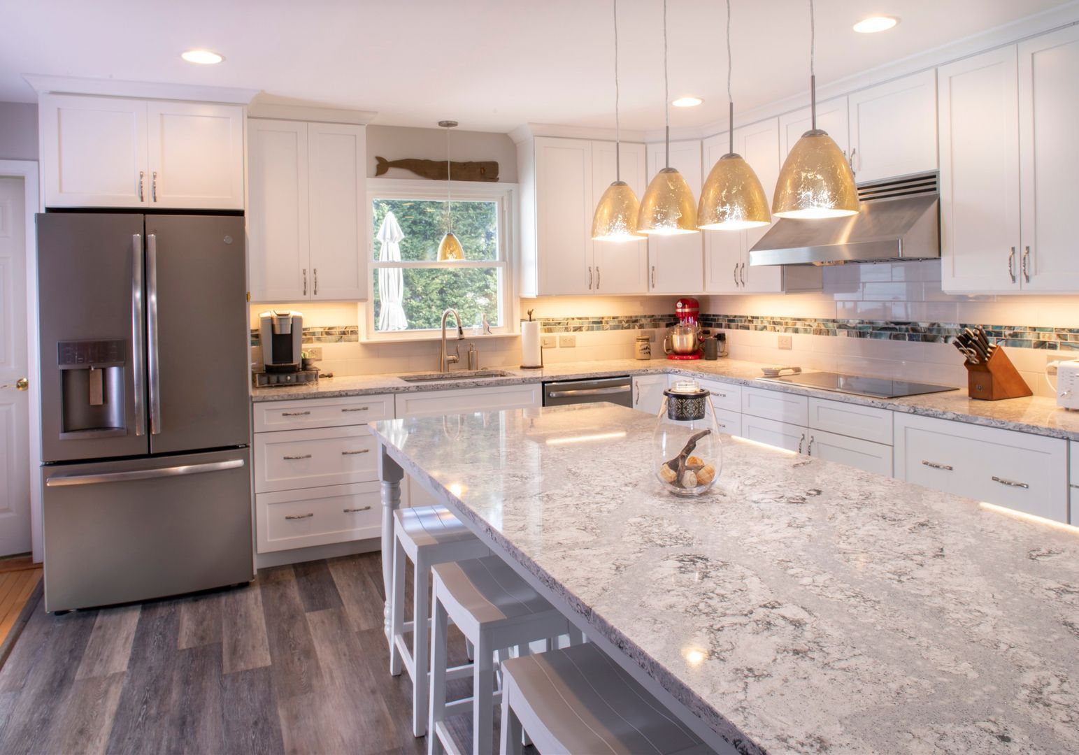 Bright modern kitchen with stainless steel appliances, white cabinets, and a marble island with pendant lights