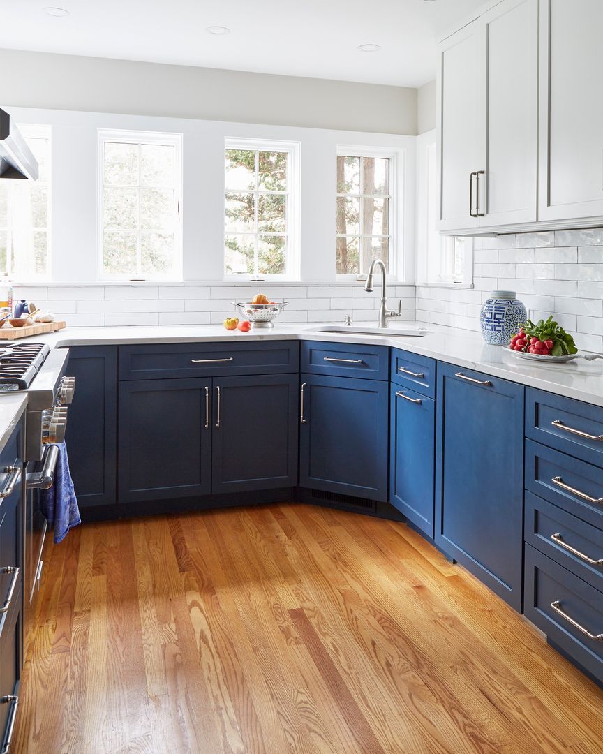Bright kitchen with navy and white cabinets, marble countertops, hardwood floor, and large sunlit windows.