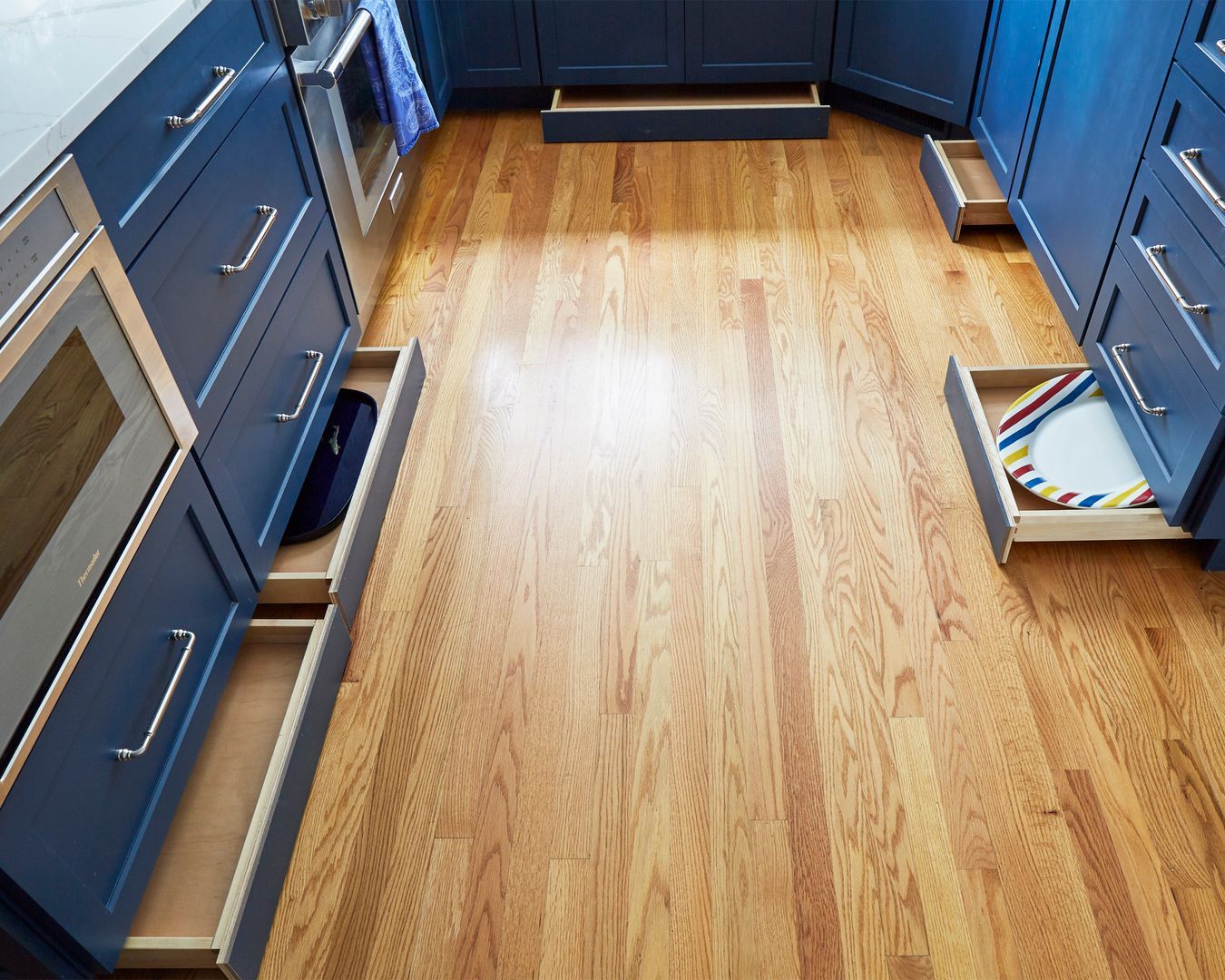 Empty kitchen with blue cabinets, hardwood floor, and a drawer pulled open on the right