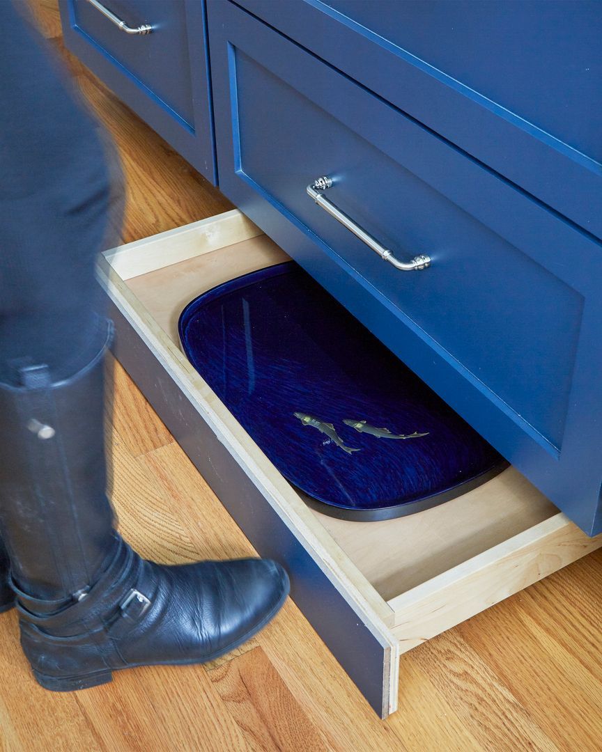 A foot pulls out a hidden drawer with a blue tray under a blue cabinet.