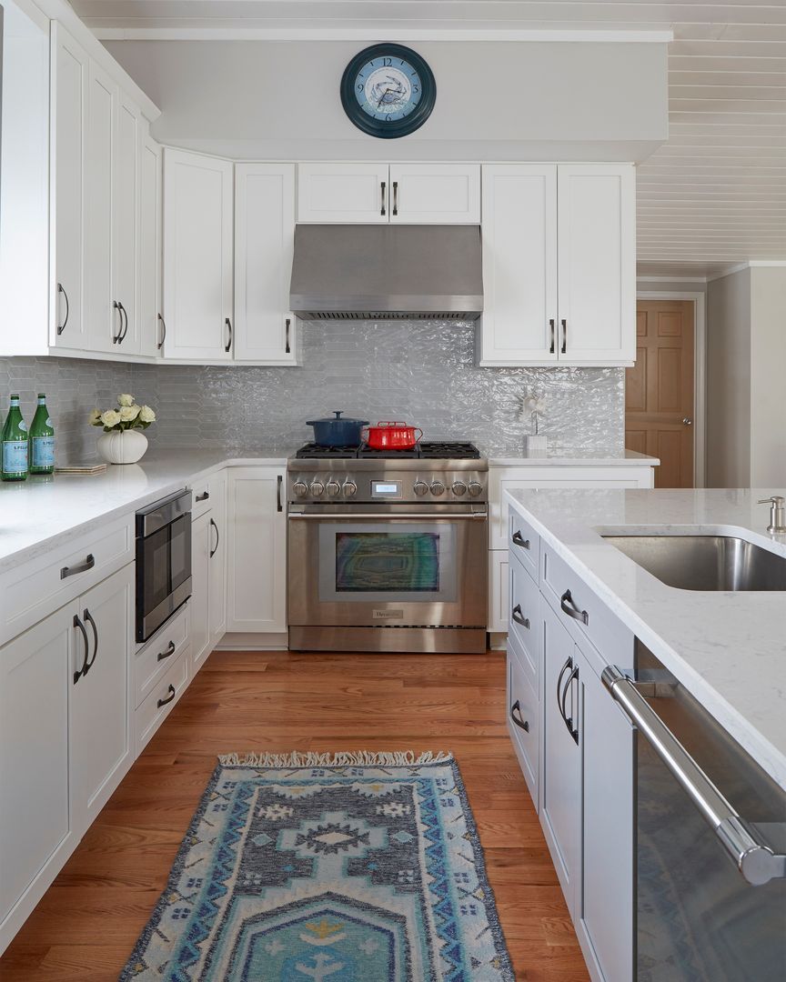 Bright white kitchen with stainless steel appliances, blue rug, and patterned backsplash.