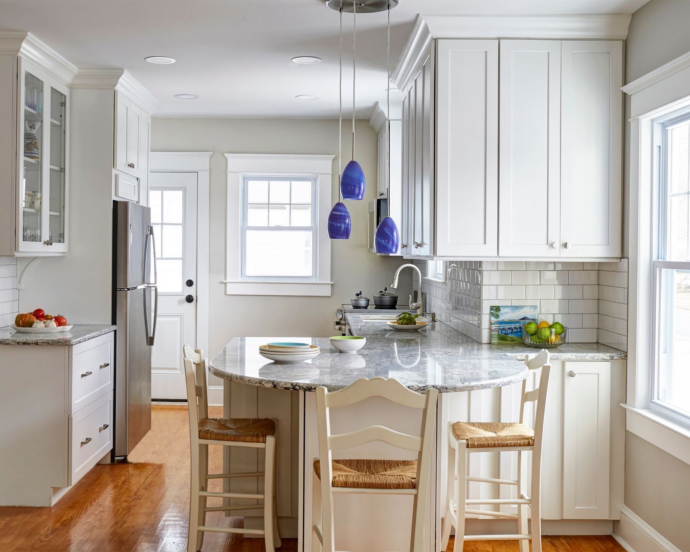Bright white kitchen with a marble island, blue pendant lights, and wooden bar stools