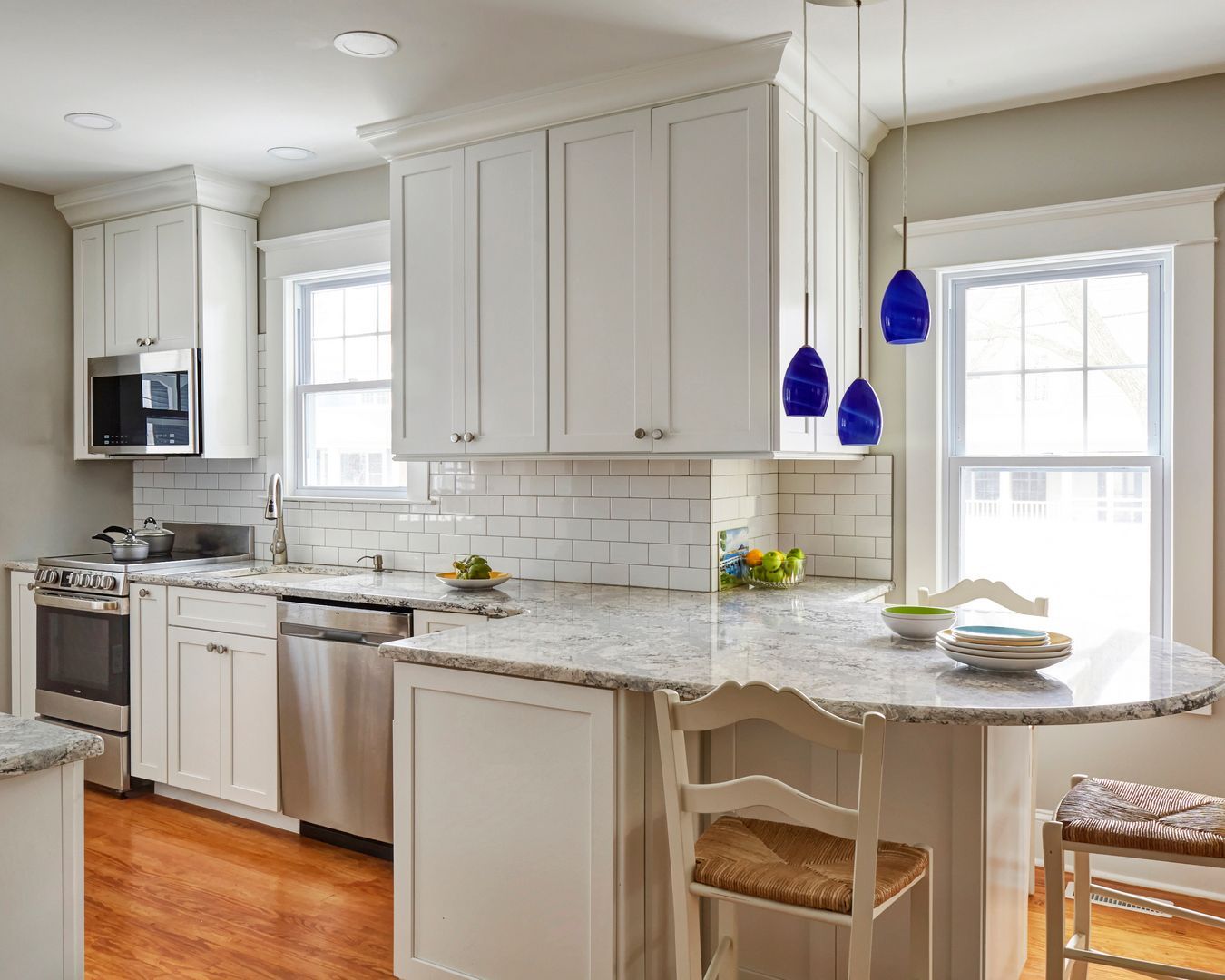 Bright modern kitchen with white cabinets, marble island, stainless appliances, and blue pendant lights