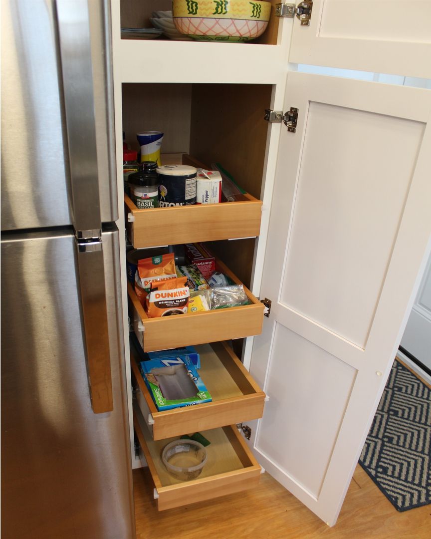 Open pantry pull-out drawers beside a stainless steel refrigerator, stocked with food and jars.