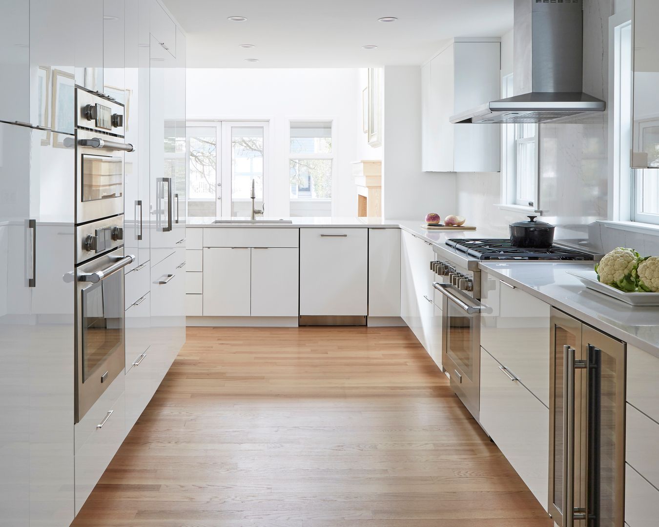 Bright modern white kitchen with stainless steel appliances, wood floor, and large windows