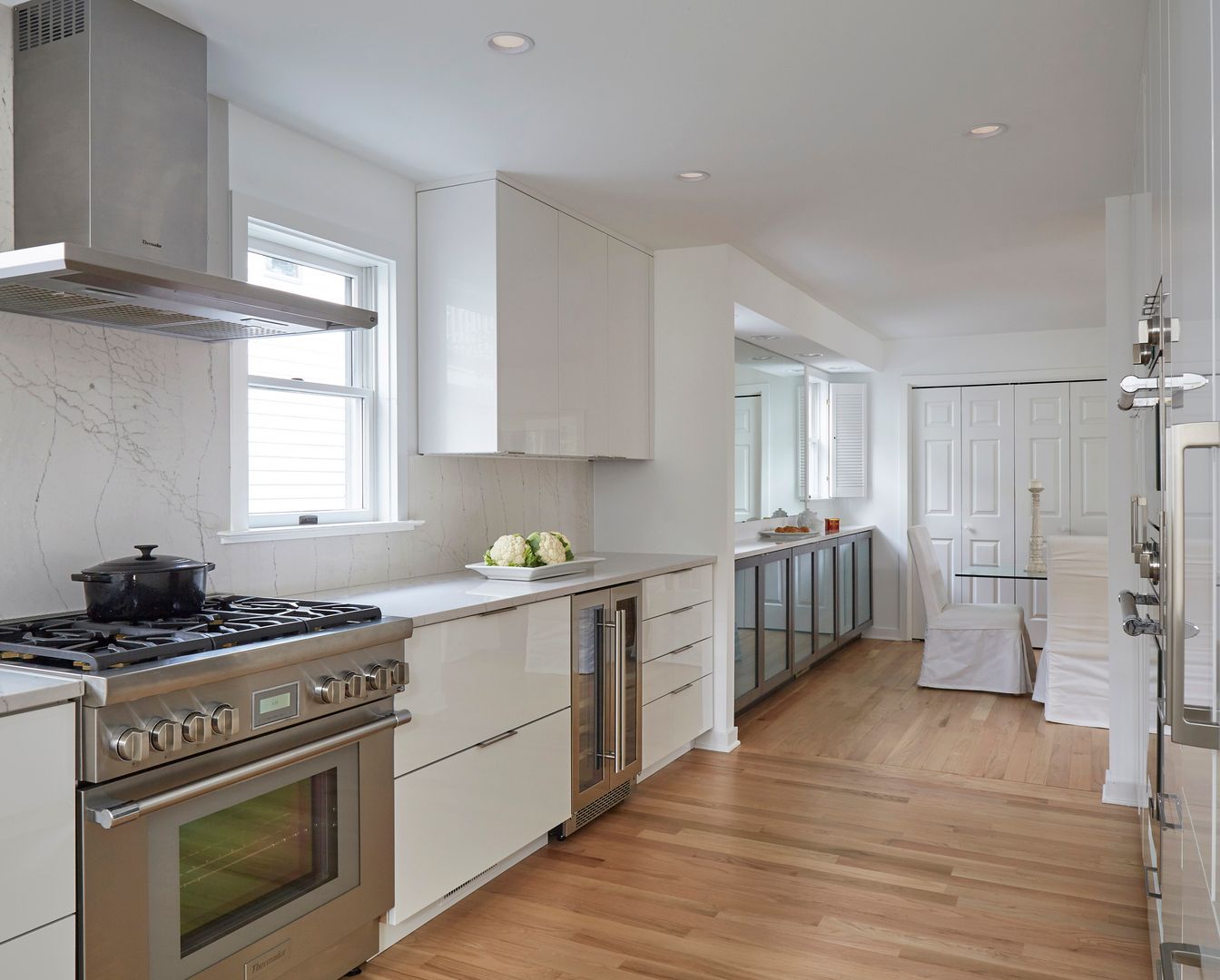 Bright white kitchen with stainless stove, wood floors, and a long counter leading to a hallway.