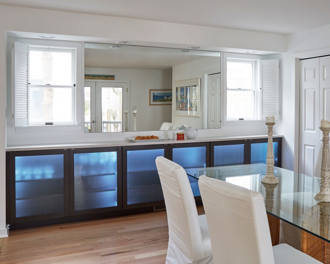 Modern kitchen with blue-lit cabinets, white chairs, and a glass dining table