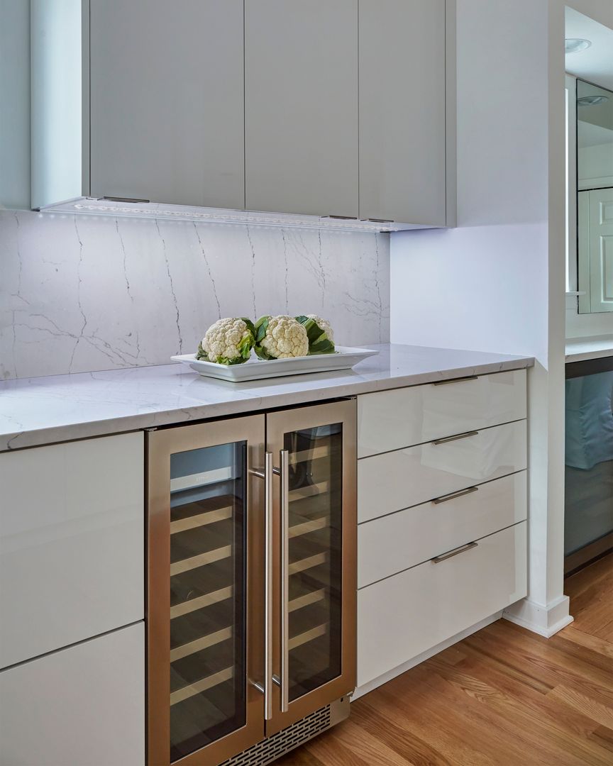 Modern kitchen with white cabinets, wood floor, and built-in wine fridge under a bright countertop.